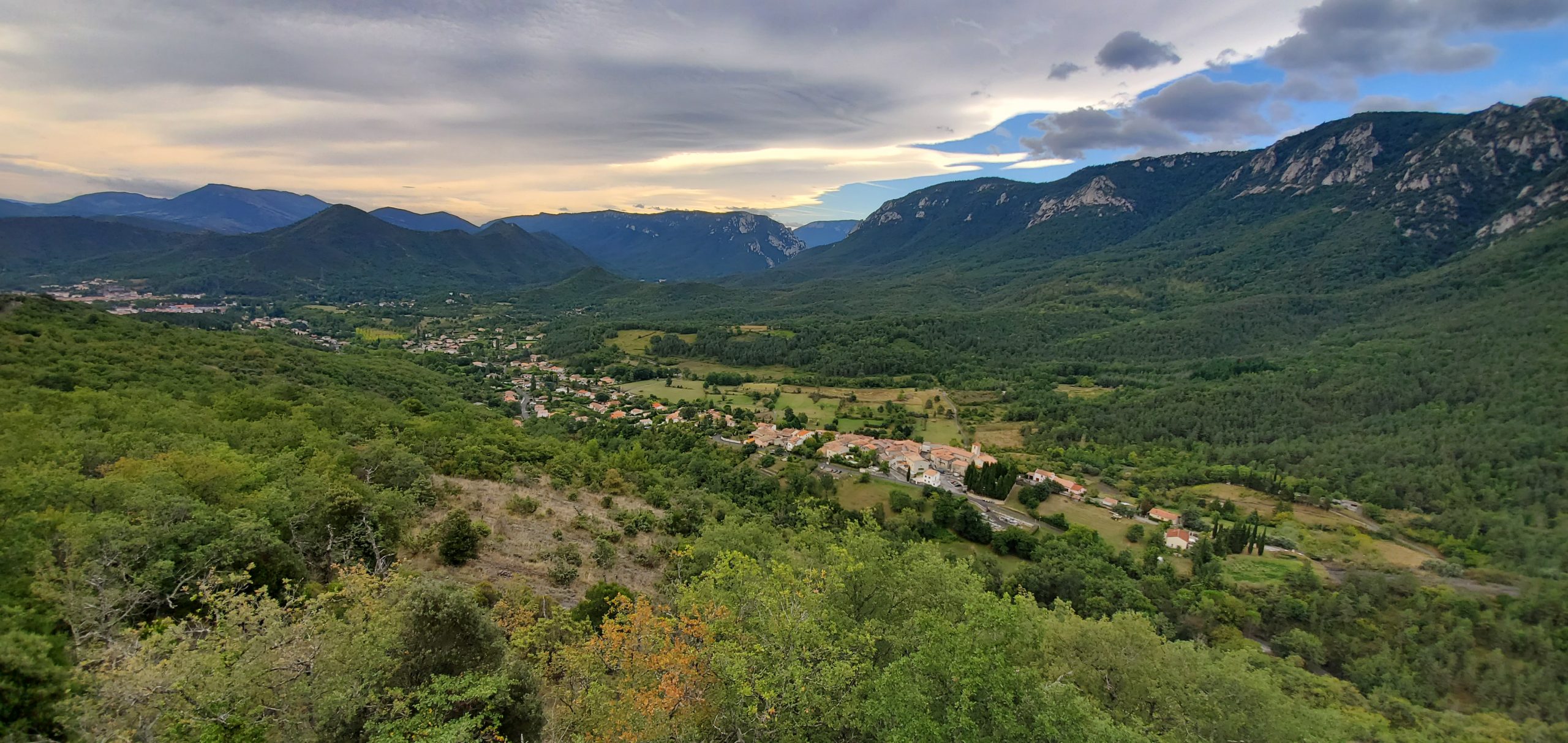 Panoramic view of a green mountain valley with winding roads and scattered villages, ideal for scenic motorcycle touring