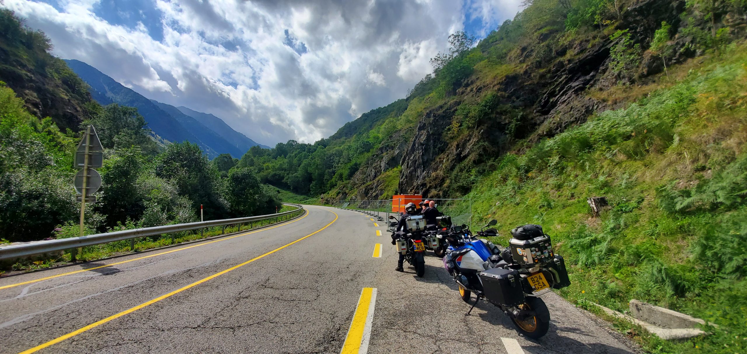 Motorcycles parked along a curvy, scenic road through the lush hills of Germany’s Black Forest under a partly cloudy sky
