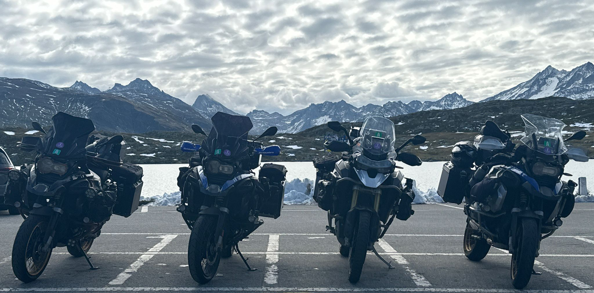 Group of touring motorcycles parked at Grimsel Pass in Switzerland with dramatic alpine peaks and snow-covered landscapes in the background