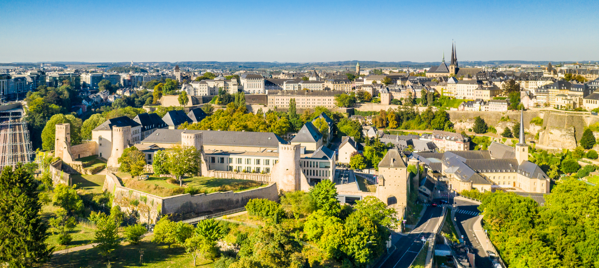 A scenic aerial view of Luxembourg City featuring historic fortifications, lush greenery, and winding roads perfect for motorcycle touring
