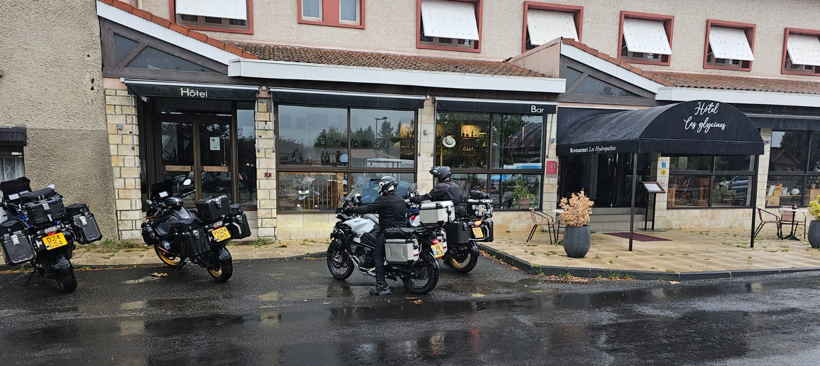 Motorcyclists parked outside Hôtel Les Glycines in France on a rainy touring day