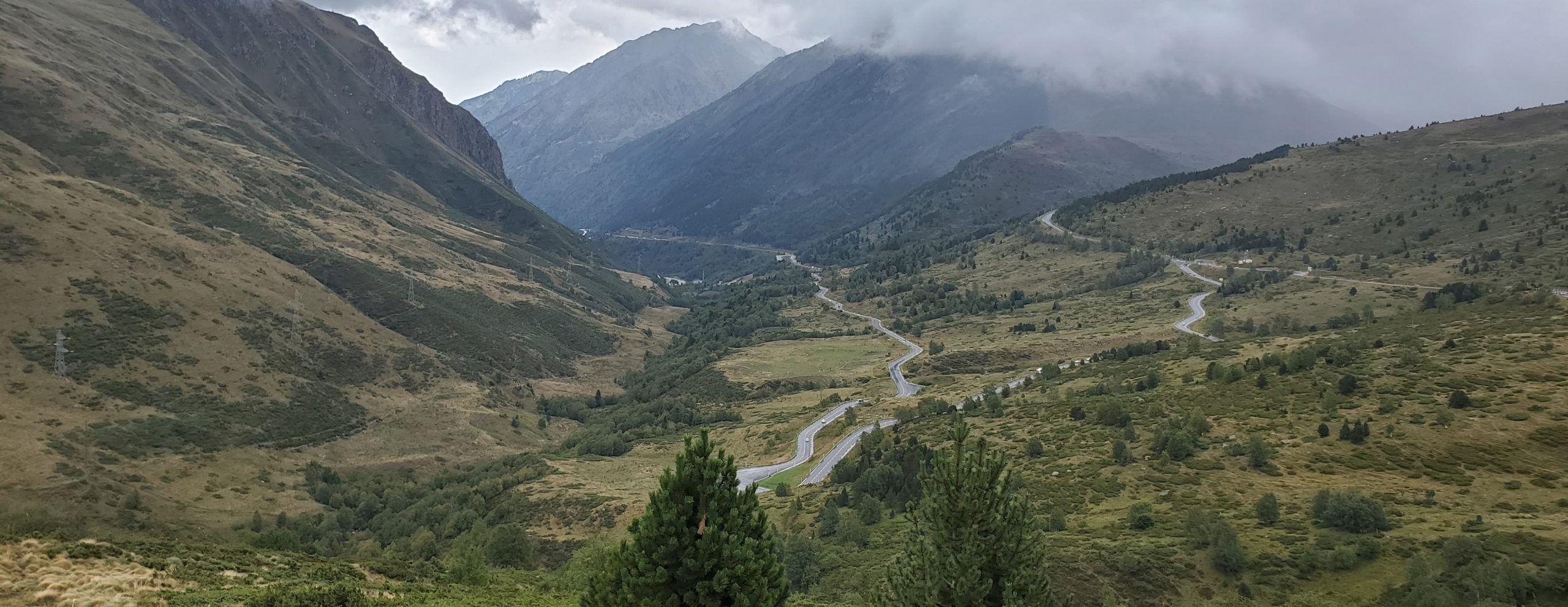 Winding mountain road crossing the Pyrenees from Spain to France under dramatic clouds.