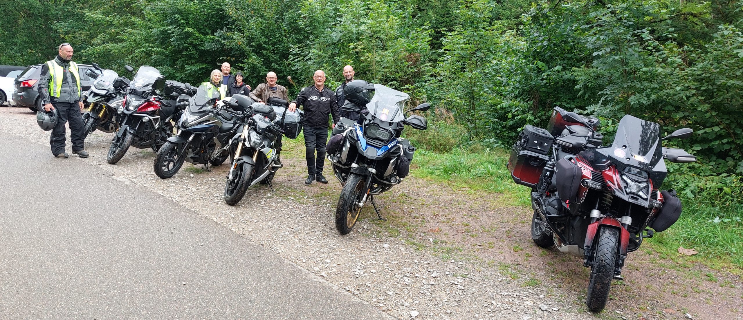 Group of motorcyclists parked on the roadside in Luxembourg, with bikes lined up and riders in gear standing nearby