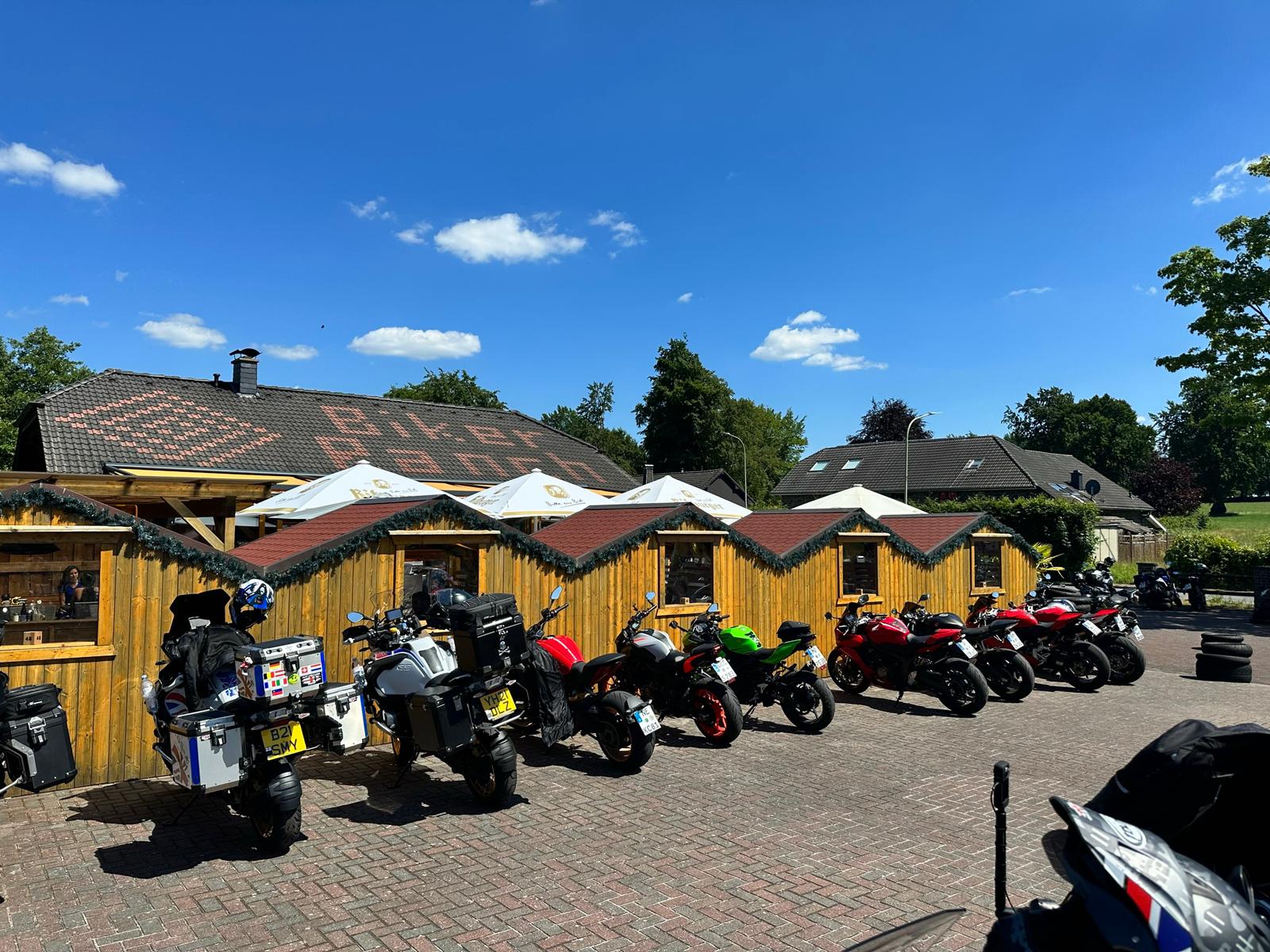 Row of motorcycles parked outside a roadside café during a 5-day beginner motorcycle tour on a sunny day.