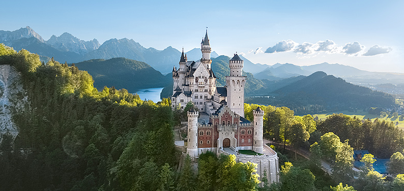 Neuschwanstein Castle perched on a hill in the Bavarian Alps surrounded by forest and mountains.